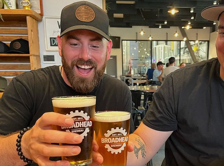 Two men holding beers with Broadhead Brewery logo on a Custom Leather Patch Trucker Hat